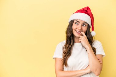 Genç beyaz kadın, sarı arka planda izole edilmiş bir şekilde Noel 'i kutluyor. Bir şeyin fotokopi odasına baktığını düşünüyor..