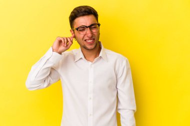 Sarı arka planda dövmeleri olan, kulaklarını parmaklarıyla kapatan, stresli ve çaresiz genç beyaz bir adam..