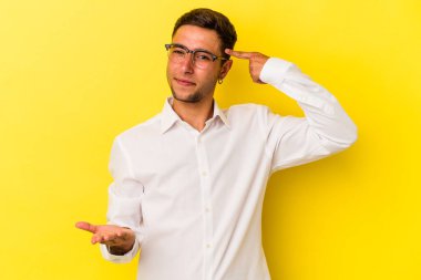 Sarı arka planda izole edilmiş dövmeleri olan genç beyaz bir adam elinde bir ürün taşıyor..