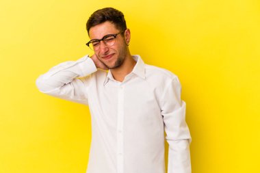 Sarı arka planda dövmeleri olan genç, beyaz bir adam stresten dolayı boynu ağrıyor, masaj yapıyor ve ona eliyle dokunuyor..