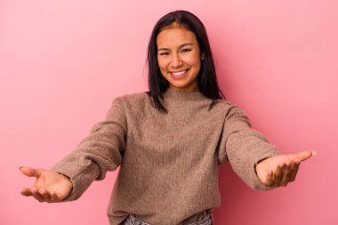 Pembe arka planda izole edilmiş genç Latin kadın hoş bir yüz ifadesi sergiliyor..