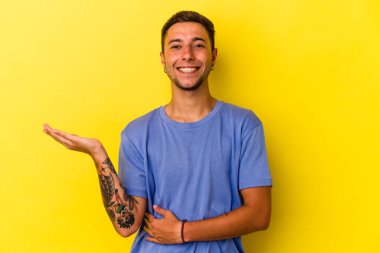 Sarı arka planda dövmeleri olan genç beyaz bir adam avuçta fotokopi alanı ve belinde bir el daha olduğunu gösteriyor..