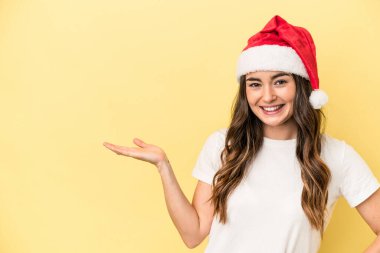 Genç beyaz kadın, sarı arka planda izole edilmiş bir şekilde Noel 'i kutluyor. Bir avuç içinde fotokopi alanı ve belinde başka bir el tutuyor..