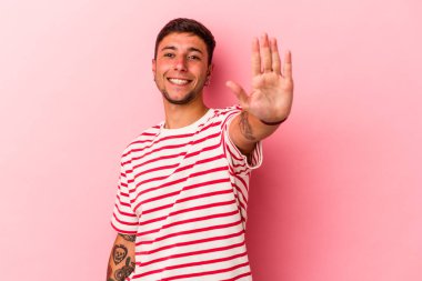 Sarı arka planda izole edilmiş dövmeleri olan beyaz bir genç adam gülümseyerek beş numarayı parmaklarıyla gösteriyor..