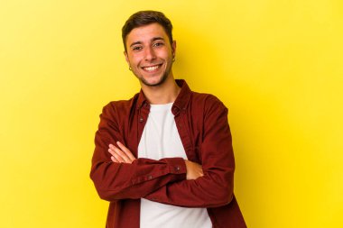 Sarı arka planda kendini güvende hisseden, kararlılıkla kollarını kavuşturan dövmeli beyaz bir genç..