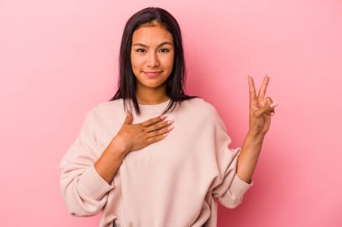 Pembe arka planda izole edilmiş genç Latin kadın yemin ediyor, elini göğsüne koyuyor..