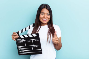 Genç Venezuelalı bir kadın mavi arka planda izole edilmiş bir alçıpan tutuyor gülümsüyor ve başparmağını kaldırıyor.