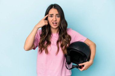 Young caucasian woman holding a motor bike helmet isolated on blue background showing a disappointment gesture with forefinger.