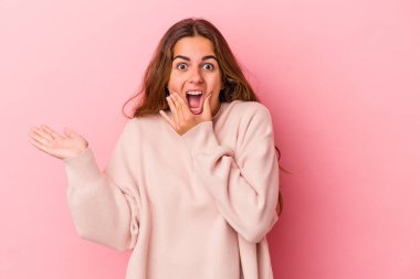 Pembe arka planda izole edilmiş genç beyaz kadın avuç içinde fotokopi alanı tutuyor, el üstünde tutuyor. Şaşırmış ve mutlu..