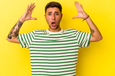 Sarı arka planda izole edilmiş dövmeleri olan genç beyaz bir adam zaferi ya da başarıyı kutluyor, şaşırıyor ve şok oluyor..