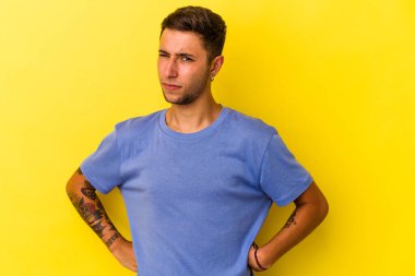 Sarı arka planda izole edilmiş, hoşnutsuzca kaşlarını çatmış, kollarını kavuşturmuş, beyaz, genç bir adam..