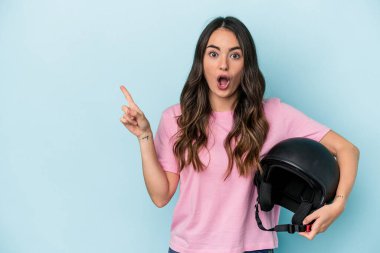 Young caucasian woman holding a motor bike helmet isolated on blue background pointing to the side