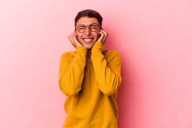 Sarı arka planda elleri kulaklarında, dövmeleri olan genç, beyaz bir adam..