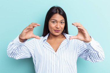 Venezuelalı genç bir kadın mavi arka planda izole edilmiş. Elinde avuç içi bir şeyle kameraya sunuyor..