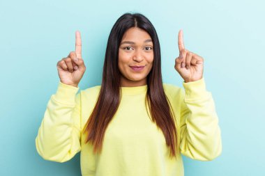 Mavi arka planda izole edilmiş genç Venezuelalı kadın iki parmağı da boş bir alan gösteriyor..