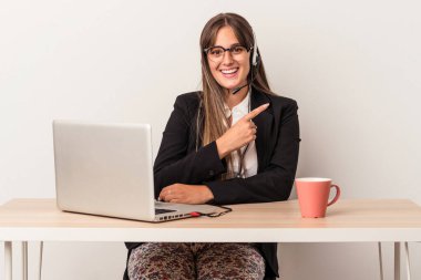 Beyaz arka planda izole bir şekilde seyahat eden beyaz tenli genç bir kadın gülümsüyor ve boş alanda bir şeyler gösteriyor..