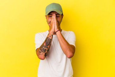 Sarı arka planda izole edilmiş, ağzı yakınında dua eden, kendine güvenen beyaz dövmeli genç bir adam..