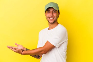 Sarı arka planda izole edilmiş dövmeleri olan genç beyaz bir adam palmiye ağacında bir kopya alanı tutuyor..