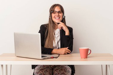 Beyaz arka planda tek başına seyahat eden, mutlu ve kendinden emin gülümseyen, elleriyle çenesine dokunan beyaz bir kadın..