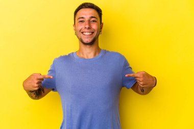 Sarı arka planda izole edilmiş dövmeleri olan beyaz bir genç. Parmakları aşağıda, olumlu hisler içinde..