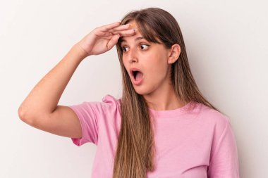 Beyaz arka planda soyutlanmış genç beyaz bir kadın çok uzaklara bakıyor ve elini alnına koyuyor..