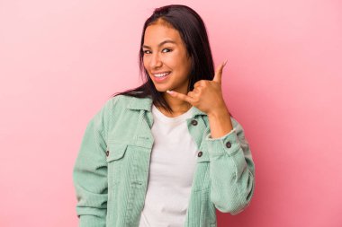 Pembe arka planda izole edilmiş genç Latin kadın parmaklarıyla bir cep telefonu hareketi gösteriyor..