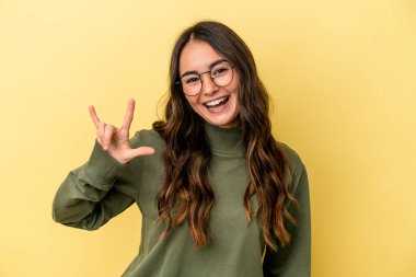 Sarı arka planda izole edilmiş genç beyaz kadın boynuzlarını devrim konsepti olarak gösteriyor..