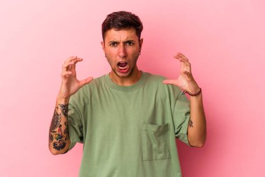 Sarı arka planda izole edilmiş dövmeleri olan genç beyaz bir adam öfkeyle bağırıyor..