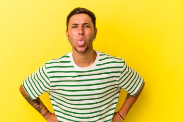 Sarı arka planda izole edilmiş beyaz dövmeli genç bir adam. Komik ve dost canlısı bir dil uzatıyor..