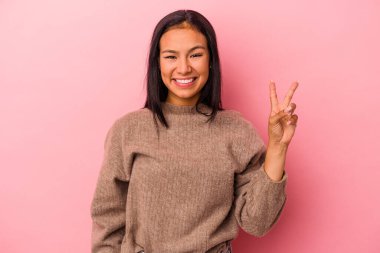 Pembe arka planda izole edilmiş genç Latin kadın zafer işareti gösteriyor ve gülümsüyor..