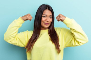 Genç Venezuelalı bir kadın mavi arka planda izole edilmiş. Güçlü bir hareket sergiliyor. Kollarıyla, kadınsı gücün sembolü.