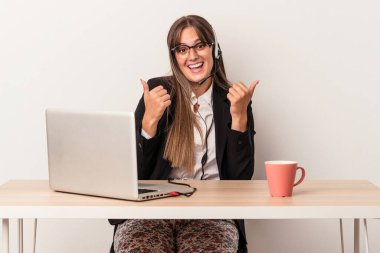 Beyaz arka planda tek başına seyahat eden beyaz bir kadın. Baş parmağını kaldırıyor, gülümsüyor ve kendinden emin..