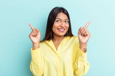 Genç Venezuelalı bir kadın mavi arka planda izole edilmiş, farklı kopya alanlarını gösteriyor, birini seçiyor, parmaklarıyla gösteriyor..