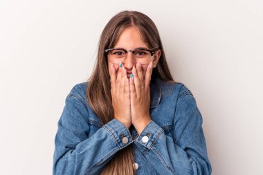 Beyaz arka planda izole edilmiş genç beyaz bir kadın bir şeye gülüyor, elleriyle ağzını kapatıyor..