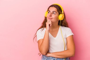 Pembe arka planda izole edilmiş müzik dinleyen beyaz bir kadın şüpheli ve şüpheci bir ifadeyle yana bakıyor..
