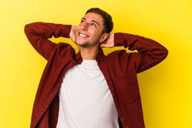 Sarı arka planda izole edilmiş, elleri başının arkasında kendinden emin dövmeleri olan genç, beyaz bir adam..