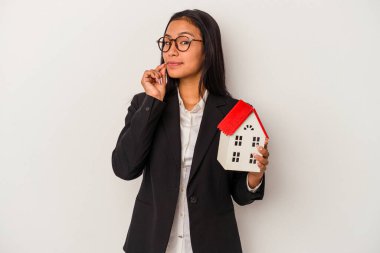 Beyaz arka planda izole edilmiş oyuncak evi tutan genç Latin kadın dudaklarında bir sır saklıyor..