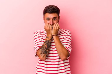 Sarı arka planda izole edilmiş, tırnak yiyen, gergin ve endişeli dövmeleri olan genç beyaz bir adam..