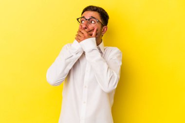 Sarı arka planda dövmeleri olan beyaz bir genç adam. Ağzını eliyle kapatan bir fotokopi odasına bakıyor..