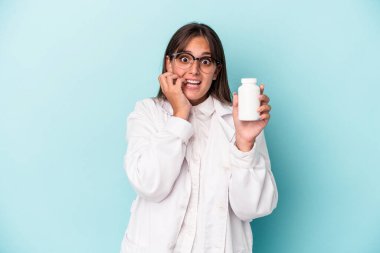 Mavi arka planda hapları tutan genç bir eczacı kadın tırnaklarını yiyor, gergin ve çok endişeli..