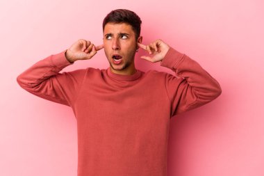 Sarı arka planda dövmeleri olan, kulaklarını parmaklarıyla kapatan, stresli ve çaresiz genç beyaz bir adam..