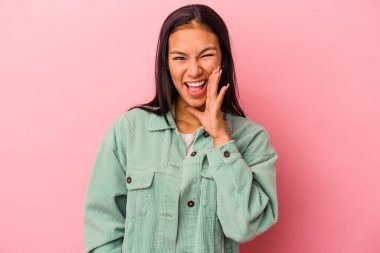 Pembe arka planda izole edilmiş genç Latin kadın yüksek sesle bağırıyor, gözleri açık ve elleri gergin tutuyor..