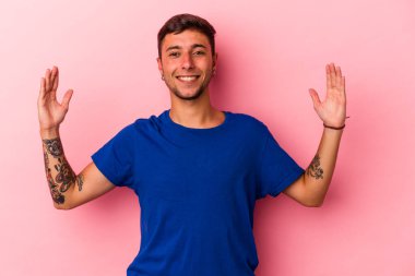 Sarı arka planda izole edilmiş beyaz dövmeli genç bir adam işaret parmaklarıyla küçük bir şey tutuyor, gülümsüyor ve kendinden emin..