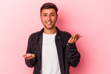 Sarı arka planda dövmeleri olan genç beyaz adam kollarıyla ölçek çiziyor, mutlu ve kendinden emin hissediyor..