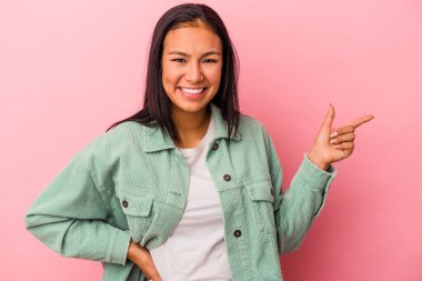 Pembe arka planda izole edilmiş genç Latin kadın işaret parmağıyla işaret ederek gülümsüyor..
