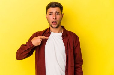 Sarı arka planda izole edilmiş beyaz dövmeli genç bir adam parmağıyla işaret ederek şaşırdı, geniş bir gülümsemeyle..