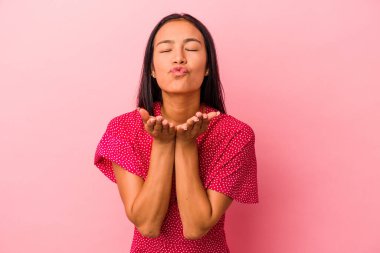 Pembe arka planda izole edilmiş genç Latin bir kadın. Dudaklarını katlıyor ve hava öpücüğü vermek için avuç içleri tutuyor..