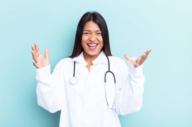 Genç doktor Venezuelalı kadın mavi arka planda izole edilmiş. Hoş bir sürpriz bekliyor, heyecanlı ve el kaldırıyor..