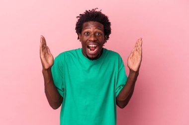 Genç Afrikalı Amerikalı bir adam pembe arka planda izole edilmiş. Hoş bir sürpriz alıyor, heyecanlı ve el kaldırıyor..