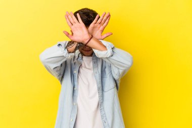 Sarı arka planda izole edilmiş, iki kolu çapraz tutan, inkar kavramı olan beyaz dövmeli genç bir adam..